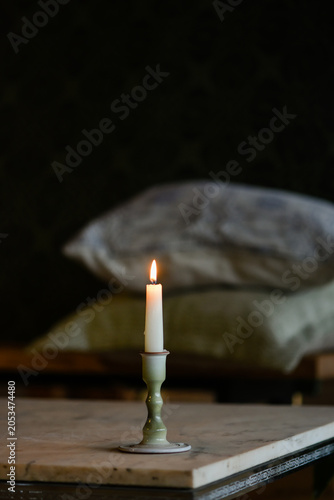 A single white lit candle in a ceramic holder casting a warm glow against a dark, rustic background.