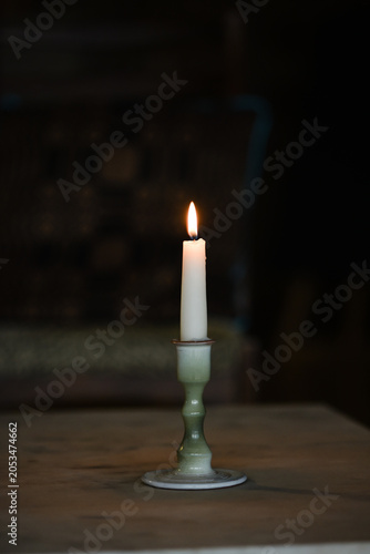 A single white lit candle in a ceramic holder casting a warm glow against a dark, rustic background.