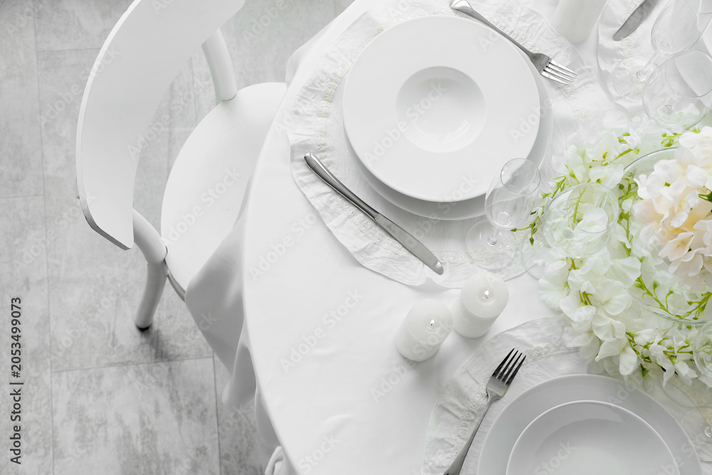 Fototapeta premium Elegant white table setting with dinnerware, cutlery, candles, and floral decor for special occasions