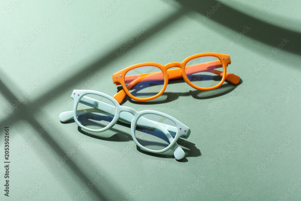 Naklejka premium Two colorful reading glasses on green background with sunlight and shadows, vision correction and eye care