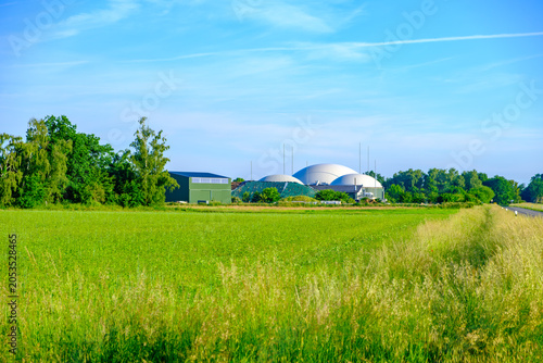 Landscape with a biogas plant, a green field, and a blue sky