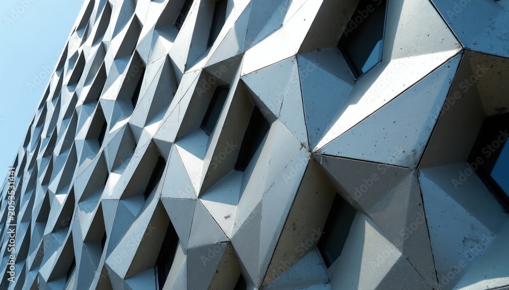 Obraz premium Modern building facade features repeating geometric diamond shapes. Angular panels create textured, abstract pattern on exterior wall. Sunlight reflects off metallic surface, casting shadows.