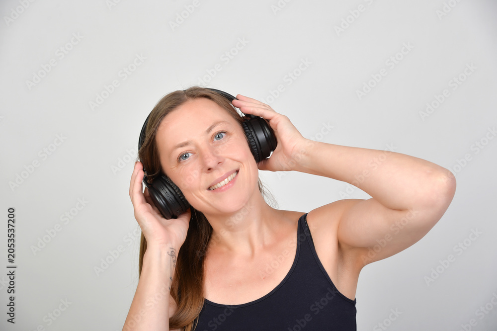 Naklejka premium Lächelnde Frau mit Kopfhörern genießt Musik und Audioinhalte. Modernes Lifestyle-Motiv für Streaming, Podcasts, Hörbücher, Entspannung, Freizeit und digitalen Medienkonsum. Echtfoto.