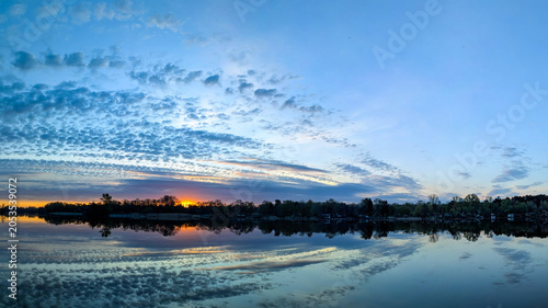 Mesmerizing sunset landscape over the river, reflecting violet reflect light in the water. Blue sky with some clouds. Dark cloud summer skies, Cloudy and clear air with copy space.