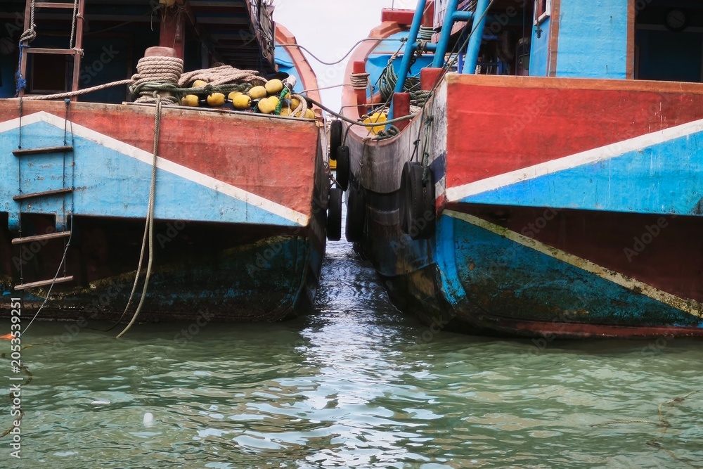 Obraz premium A symmetrical, eye-level shot of two weathered wooden fishing boats moored side-by-side, their hulls painted in vibrant, faded tones of red and blue with white chevron accents.