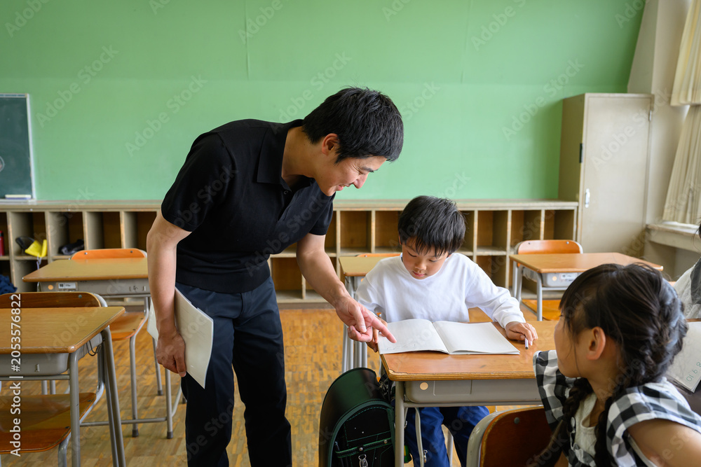 Fototapeta premium 教室で勉強する女子小学生を傍で見守る男性教師