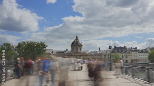 Time lapse shot of Institut de France in distance as blurred people walk across bridge in foreground. 