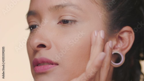 Big close-up shot of latin woman tan skinned strokes her forehead and cheek revealing nourished skin on tan background | Face care commercial