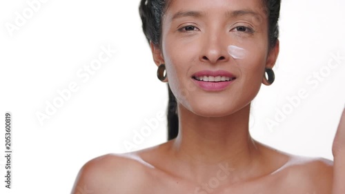 Close-up shot of hispanic woman with light brown smooth skin applying cream on her cheek on clean white background | Skin care commercial concept