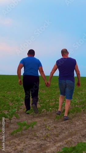 An emotional embrace of two handsome mature men walking in nature. A happy gay couple on a walk in a field, having a fun time. Vertical video.