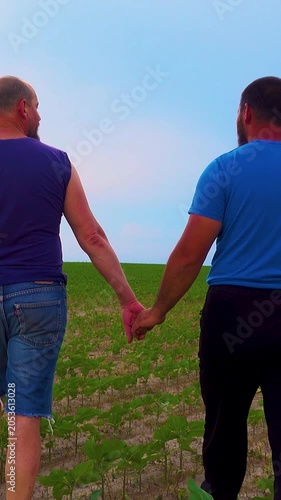 An emotional embrace of two handsome mature men walking in nature. A happy gay couple on a walk in a field, having a fun time. Vertical video.