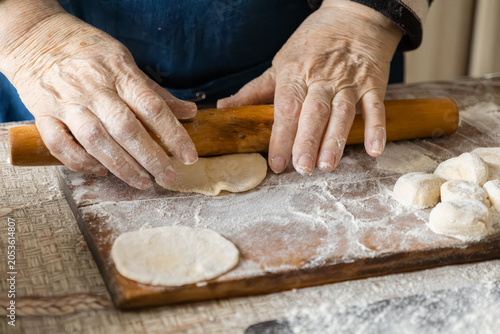 Fotografía Elderly person hands rolling dough with a wooden pin on a floury board, preparin
