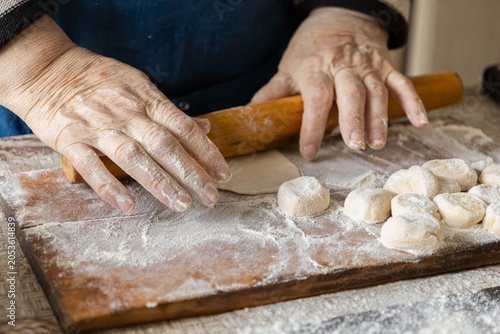 Foto Elderly hands use a wooden rolling pin to flatten dough on a floured surface, pr