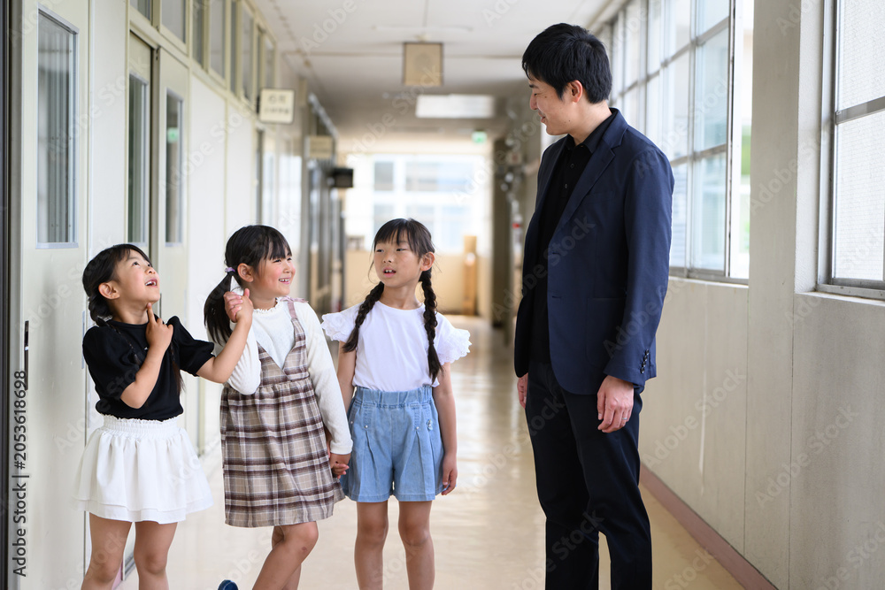 Fototapeta premium 学校の廊下で男性教師と和やかに会話をする女子小学生のグループ