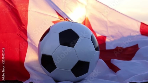A soccer ball rests on a Canadian flag with a field background during a beautiful sunset. It symbolizes Canada hosting the World Cup 2026 with USA, inspiring futbol fans for sports