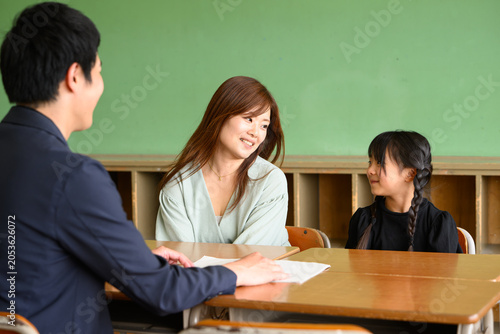 教室で先生と和やかに三者面談をする母親と女子小学生