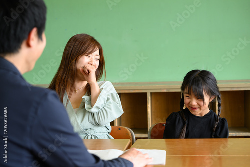 教室で先生と和やかに三者面談をする母親と女子小学生