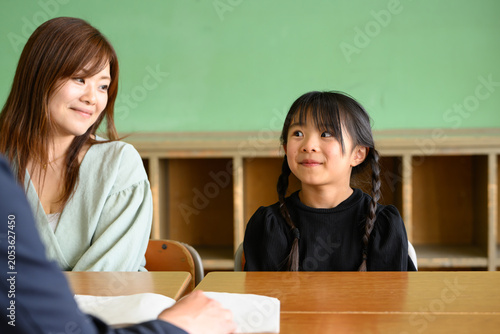 教室で先生と和やかに三者面談をする母親と女子小学生
