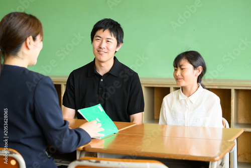 教室で先生と和やかに三者面談をする父親と高学年の女子小学生