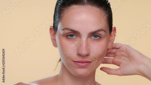 Headshot of fair-skinned bule-eyed beauty model confidently strokes her jawline presenting well hydrated skin on neutral background