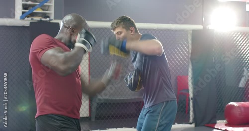 Diverse male coach and trainee on coach signal practicing focus mitt combos in cage for training