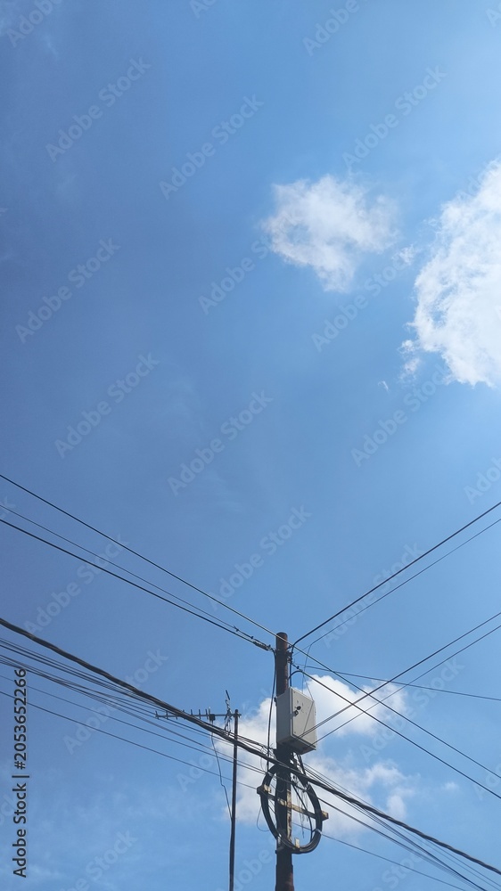 Fototapeta premium Electrical and Fiber Network Installation on Utility Pole Under White Clouds and Blue Sky, Modern Infrastructure and Connectivity Background