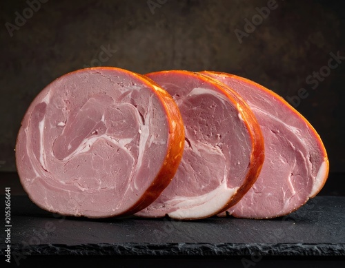 Sliced, cured pork roast with swirls of fat, presented on dark slate