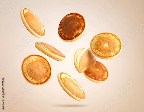 Several small, golden-brown circular food items are suspended in mid-air against a soft, gradient background