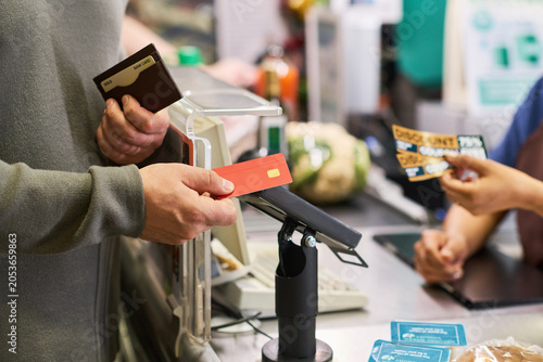 Fotografi Adult customer holding payment cards and completing grocery checkout with supermarket worker, showing retail purchase transaction