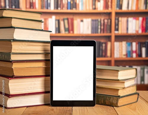 Stacked books and a blank tablet PC stand before a library bookshelf
