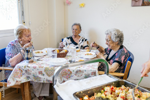 Canvas Print Senior residents dining together at a table in a care facility, eating healthy f