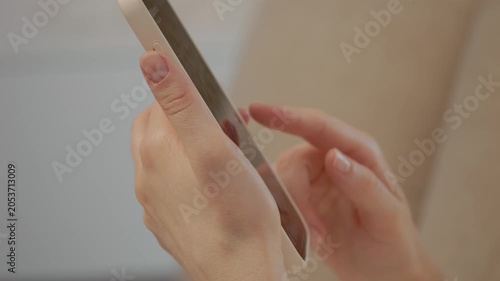 A woman holds her phone and swipes through social media while sitting at home. She interacts with friends online and enjoys the moment in her living space.