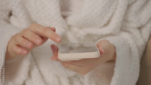 A woman is holding a smartphone while swiping through the screen. She is socializing at home. Her hands are relaxed and engaged with the device.