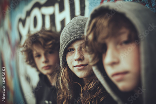 Three young friends with hooded sweatshirts pose against a vibrant graffiti wall, exuding a cool vibe.