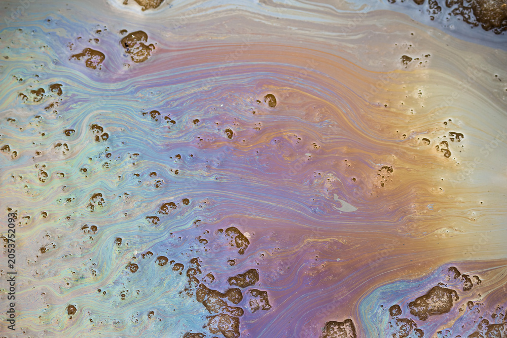 Naklejka premium Iridescent oil slick patterns swirling on melting spring slush, toxic chemical residue and gasoline stains creating vibrant rainbow texture on wet asphalt surface, environmental pollution concept