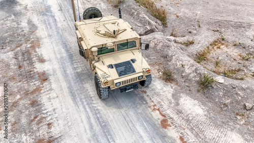 Military vehicle moves on dirt road in a training area during daylight hours