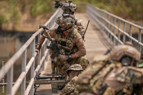Military personnel conduct training on a bridge in a forested area during the day