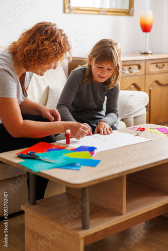 Mother and daughter cutting and gluing collage paper while doing an art project at home for school
