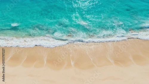 Aerial view of a pristine tropical beach with turquoise ocean waves gently lapping the golden sand.