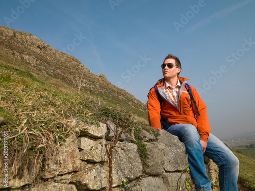 Canvastavla Young man in orange jacket sitting on hilside admiring the view