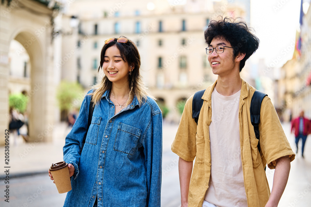 Fototapeta premium Portrait of a smiling couple walking down the street in the city, tourists visiting destination, summer trip exploring