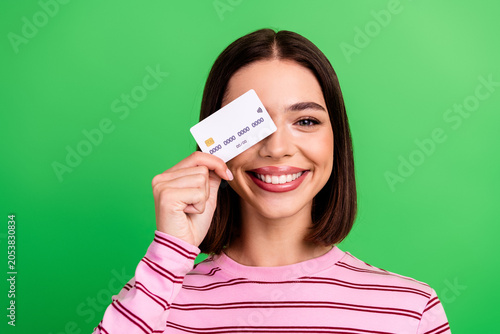 Quadro su tela Young chic woman holding a credit card smiling against a green background wearin