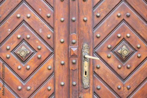 Ornate wooden door with diamond patterns and decorative metal studs, featuring a vintage brass handle and keyhole, showcasing craftsmanship and intricate design details