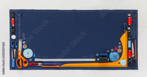Frame from sewing accessories and supplies on blue fabric background on white table. DIY concept. Tailoring, embroidery and sewing as a hobby. Flat lay, closeup, top view, banner, copy space,  blank