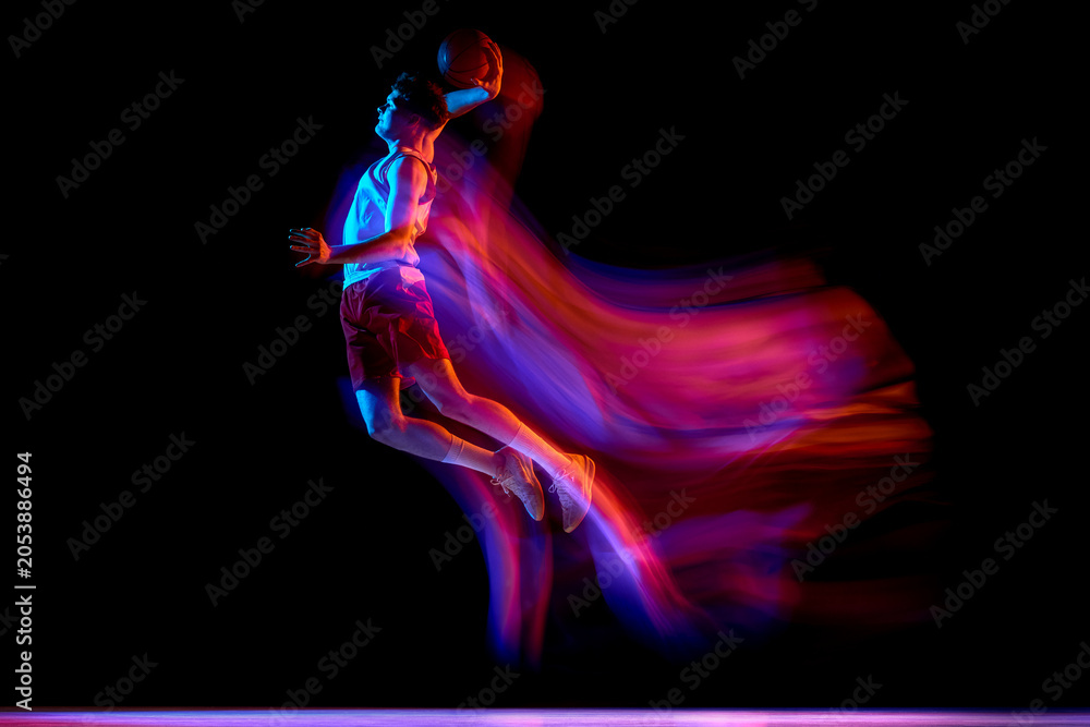 Naklejka premium Basketball player jumping with neon motion blur on black studio background. Concept of basketball performance, sport advertising, energy drink campaign, speed, power, event poster.