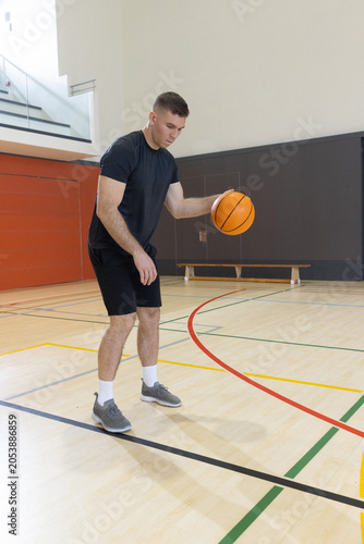 Male basketball player is dribbling orange ball on hardwood court near red wall panels