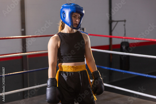 Boxer is pausing in boxing ring, wearing blue headguard and black gloves near heavy bag