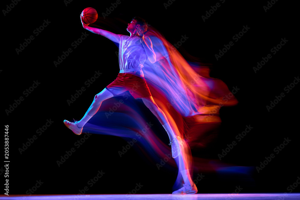 Naklejka premium Basketball player leaping forward with neon trails on dark studio background. Concept of basketball performance, sport advertising, poster design, power, energy, scoring action.
