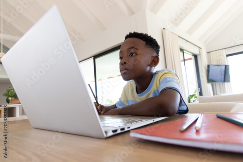 Photos African American school-age boy in striped tee studying at wooden table at home