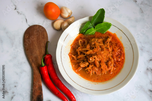Spicy young papaya curry served in a rich coconut milk sauce, garnished with kaffir lime leaves and accompanied by fresh chili peppers. isolated on white marmer.